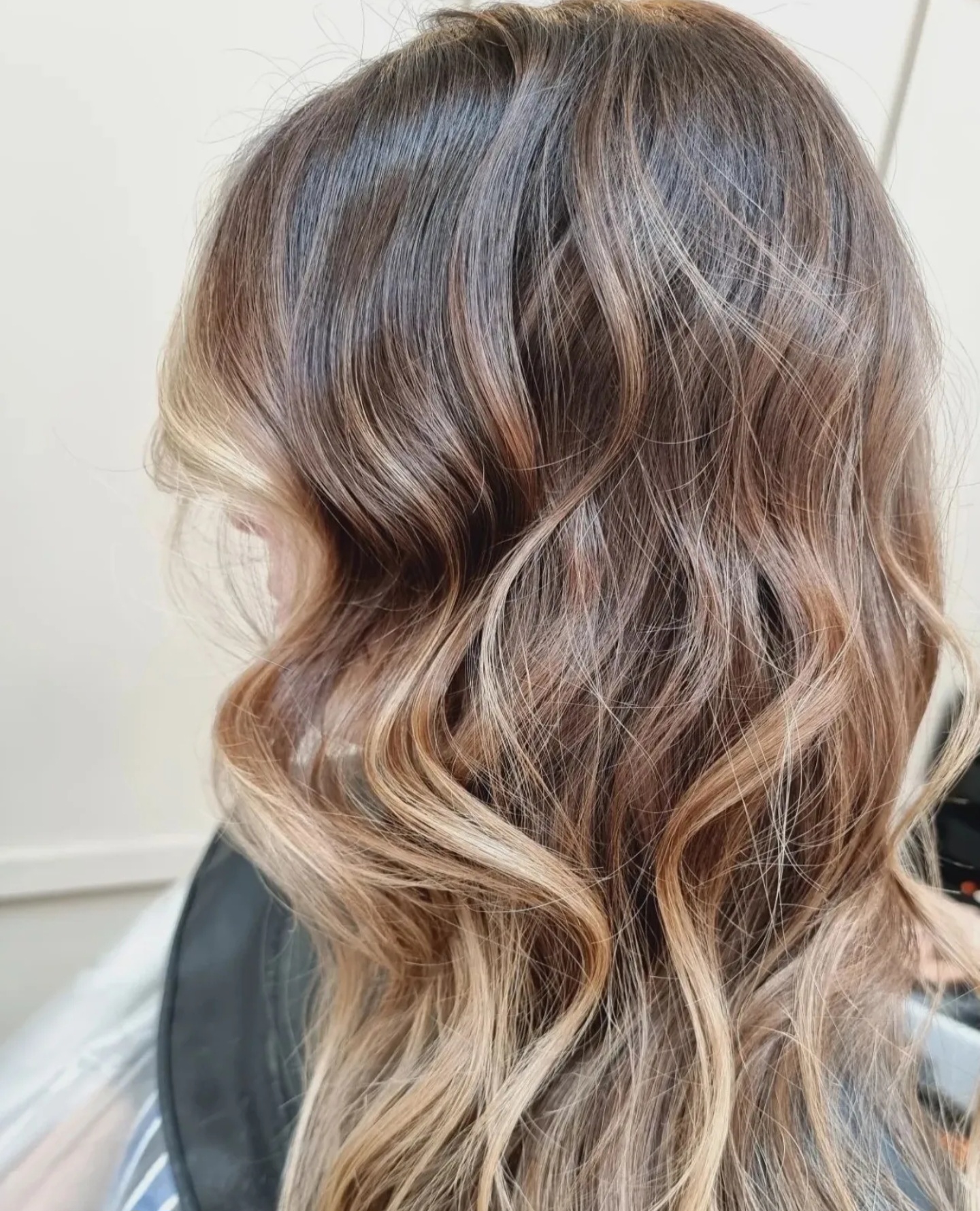 Side profile of long wavy hair with soft light-brown balayage colour by TONES Lahore
